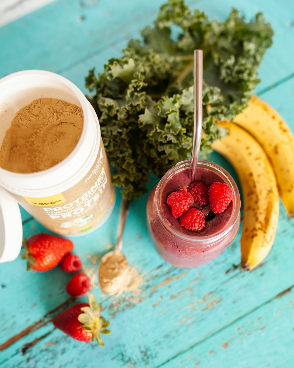 Protein powder, bananas, kale, and a berry smoothie on wood.