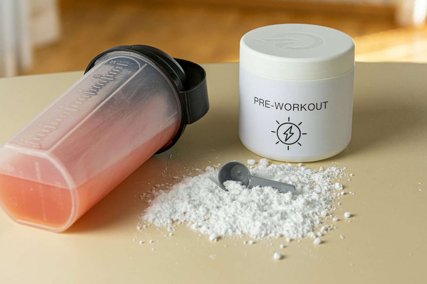 Pink pre-workout drink in shaker bottle next to tub of powder.